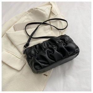 Detail of black pleated cloud bag with silver hooks on a beige blazer background