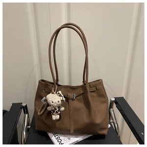 Detail of brown tote bag with long strap and cute plush charm on a modern leather chair