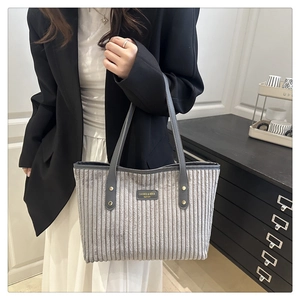 Detail of grey corduroy tote bag with leather strap and metallic brand emblem