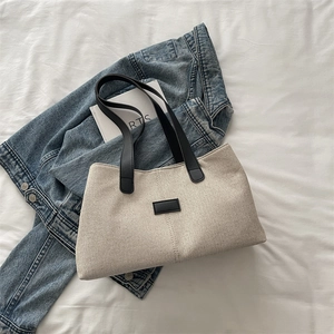 Minimalist beige woven tote bag with black handles and leather patch on white fabric