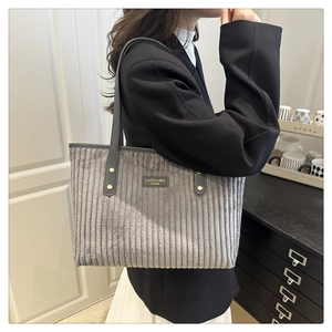Detail of grey corduroy tote bag with leather straps and logo badge on model side view