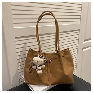 Detail of a brown leather tote bag with a plush cat charm on a white book