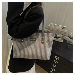 Close-up of dark grey corduroy tote bag featuring leather logo patch and metal rivets