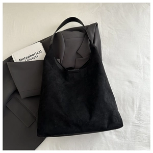 Détail du sac hobo en daim noir posé sur un tissu de costume gris foncé