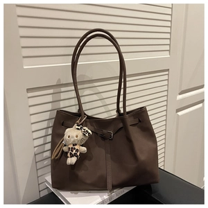 Close-up of a coffee brown tote bag featuring a plush kitty pendant and metal buckle details