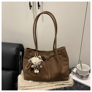 Detail of a brown vintage tote bag with a plush bear charm on a soft knit fabric