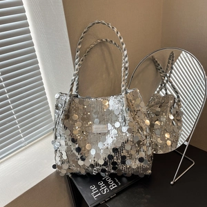 Silver sequin tote bag with woven handles and fashion tag on a book in sunlight