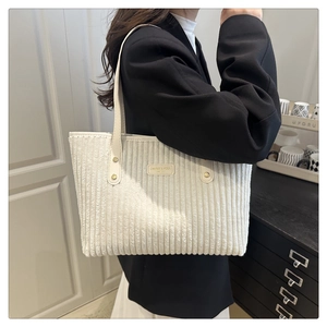 Detail of white corduroy tote bag featuring vertical texture and golden rivet strap accents