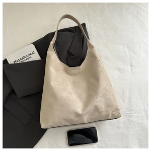 Détail du grand sac cabas en daim beige minimaliste posé sur un tissu texturé blanc