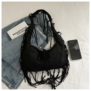 Close-up of black fringe hobo bag with long tassels on white textured bedding