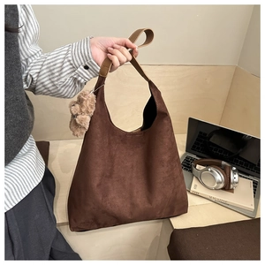 Détail d'un sac hobo en daim marron mat avec un charm ours en peluche dans un décor