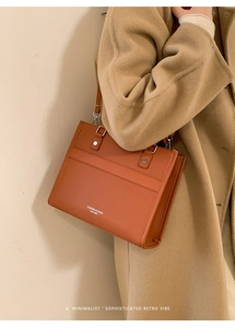 Close-up of brown leather tote bag with embossed text worn with a beige wool coat