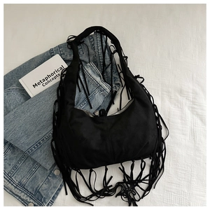 Close-up of black suede hobo bag with fringe tassels on white bedsheet texture