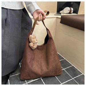 Dettaglio della borsa tote in pelle scamosciata marrone con manici e ciondolo a orsetto