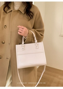 Dettaglio della borsa in pelle crema con eleganti manici e tracolla regolabile