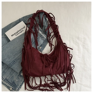 Macro detail of wine red suede shoulder bag with bohemian fringe and tassel accents