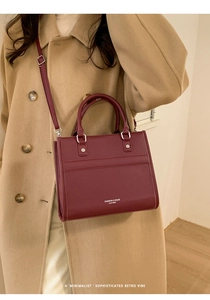 Dettaglio della borsa in pelle bordeaux con manico e testo moda indossata da modella