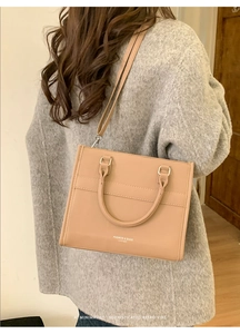 Close-up of khaki leather tote bag showing adjustable straps and fine litchi texture