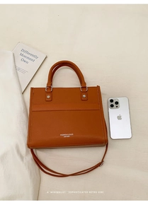 Detail of terracotta leather crossbody bag with logo lettering and pebble grain texture