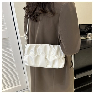 Close-up of a white pleated shoulder bag with cloud texture on a model in a suit