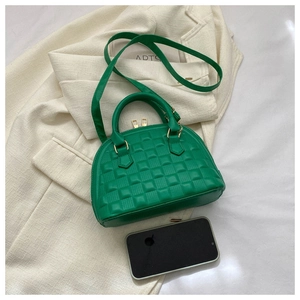 Vista superior del bolso acolchado verde con herrajes dorados junto a un teléfono móvil