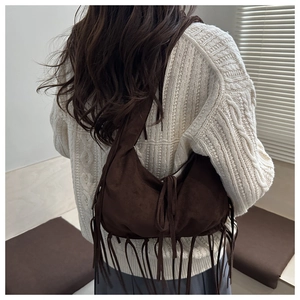 Detail view of dark brown suede shoulder bag with long fringes on a white knit sweater