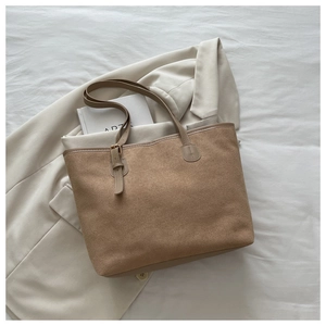 Detailed macro view of brown suede tote bag with slim shoulder straps on light fabric