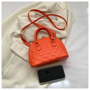 Vista superior del bolso de mano naranja tipo concha con acolchado sobre un blazer