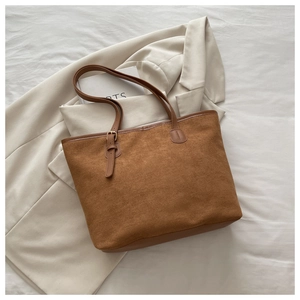 Flat lay of caramel tote bag on beige blazer showing texture and metal buckle detail
