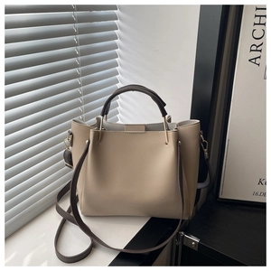 Close-up of beige lychee-textured leather bag with brown handles and gold hardware