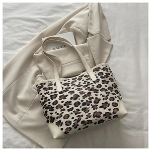 Top view of a leopard print canvas tote bag with cream leather trim on a stylish bed