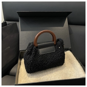 Close-up of black teddy faux fur bucket bag with brown resin handle and leather flap