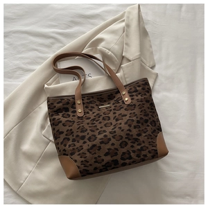 Detail view of leopard print tote bag featuring brown leather trim and metal accent