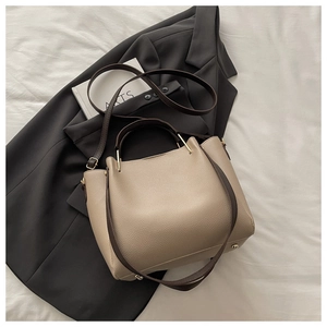 Detailed view of beige pebble leather tote bag with protective metal feet and brown strap