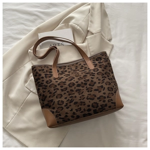 Detailed view of leopard print tote bag with brown leather handles on white fabric