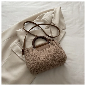Detail of plush brown bucket bag with round wooden handle and leather strap on beige blazer