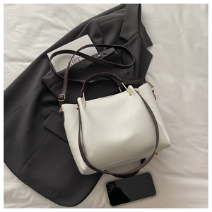 White lychee leather tote bag with brown straps styled on white fabric with office attire