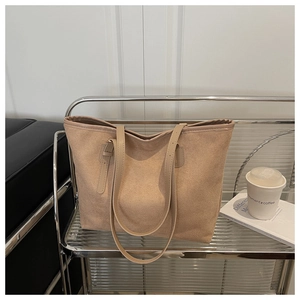 Close-up of beige suede tote bag with leather strap and metal buckle on display stand