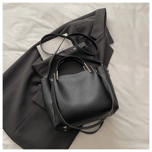 Detail of black pebbled leather tote bag featuring gold hardware and protective base studs