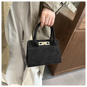 Dettaglio di borsa nera opaca con design a trapezio e chiusura in metallo dorato lucido