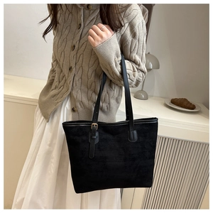 Detail of a minimalist black suede tote bag featuring adjustable strap and golden buckle