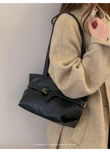 Dettaglio di una borsa a spalla retrò nera con fibbia dorata su un cappotto beige