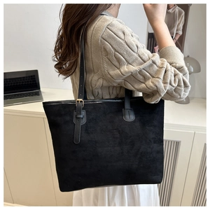 Minimalist black suede tote bag with gold buckle on shoulder strap in office setting