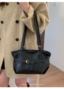 Dettaglio borsa sottobraccio in pelle nera minimalista con fibbia dorata su cappotto beige