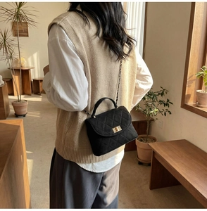 Detail of quilted crossbody bag with gold chain strap shown on model in cozy room