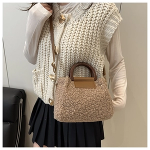 Detail of a khaki faux fur bucket bag with a brown leather handle shown on a model