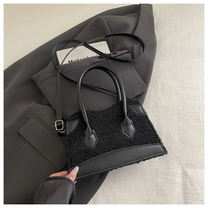 Détail du sac à main noir en peau de mouton et cuir posé sur une veste de costume grise