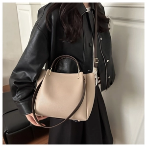 Dettaglio di una borsa a secchiello beige con manici marroni indossata da una modella