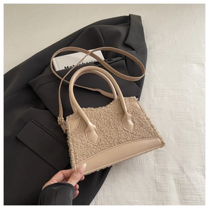 Détail du sac à main beige en polaire avec poignée en cuir sur un blazer noir