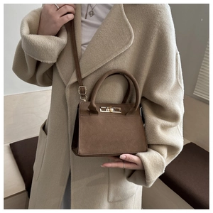 Sac à main trapèze en daim marron avec fermoir doré porté sur un manteau en laine